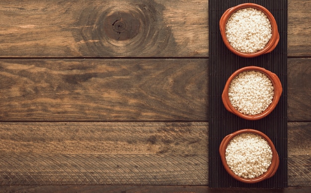 Free Photo white rice of uncooked bowls on placemat over the wooden background