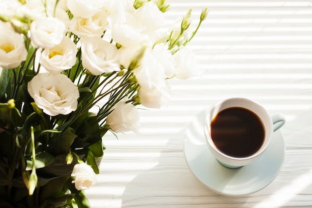 Free photo white rose bouquet with black coffee cup on desk