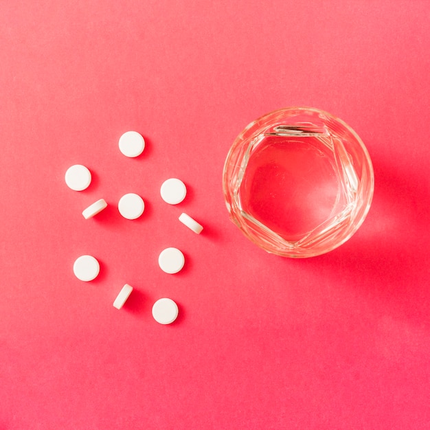 Free photo white round pills and glass of water on red background