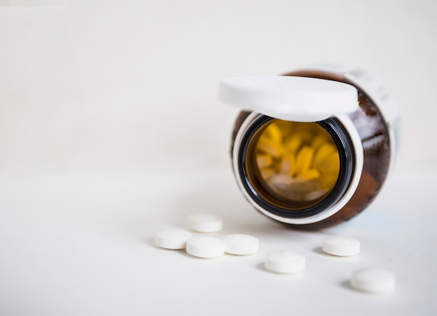 Free photo white round pills spilling from brown bottle on white background