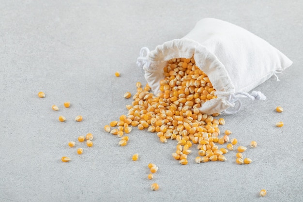 Free photo a white sack full of corn grains on a gray surface.