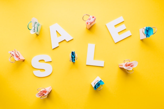 Free Photo white sale alphabet surrounded with miniature shopping bags on yellow backdrop