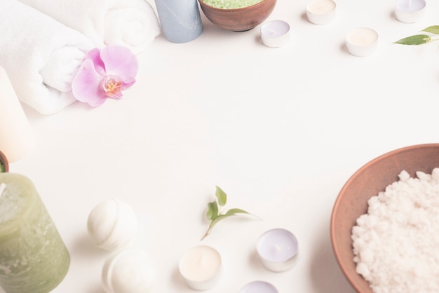 White sea salt, candles, rolled up towel, spa bomb on white background