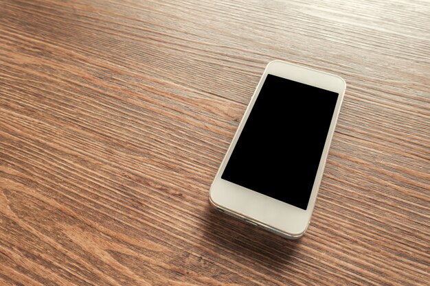 White smart phone with blank screen on wooden desk