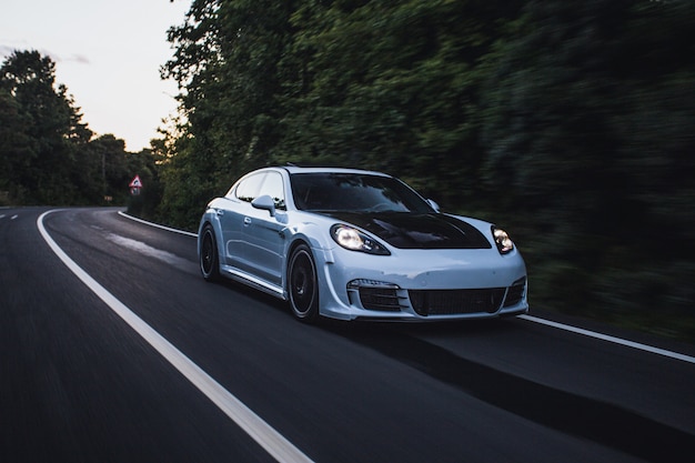 A white sport car with black autotuning driving by the forest.