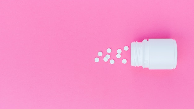 Free Photo white tablets spilled from the plastic bottle on pink background