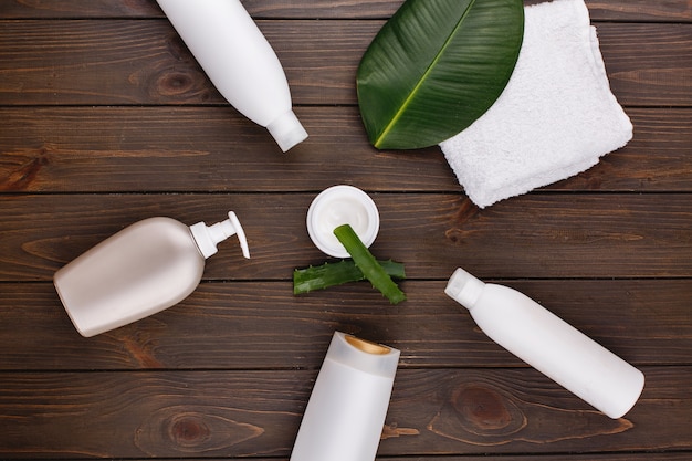 White towel, bottles of shampoo and conditioner lie on a table with green leaf and aloe