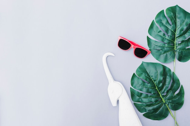 Free photo white unicorn, sunglasses and green monstera leaf over grey backdrop