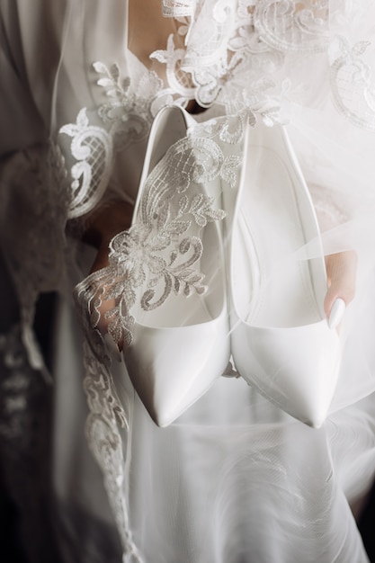 Free Photo white wedding ceremonial shoes in the hands of bride dressed in silk nightwear with lace