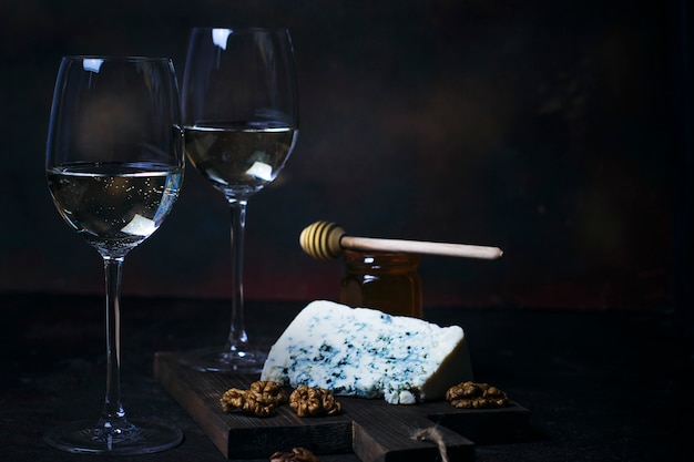 Free Photo white wine in fine glass with blue cheese, honey, walnuts on dark 