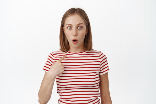 Free Photo who me surprised blond girl student looking in disbelief and awe at camera pointing at herself being chosen winning something achieve prize staring shocked white background