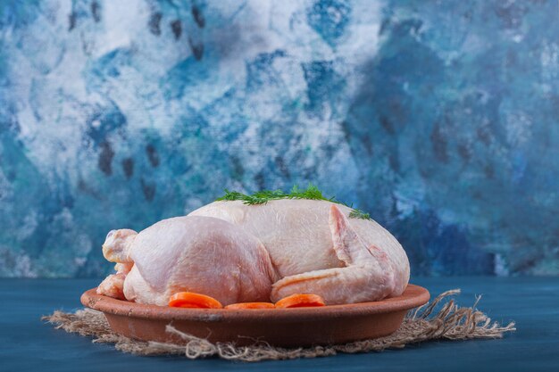 Whole chicken and sliced carrots on a plate on a burlap napkin on the blue surface