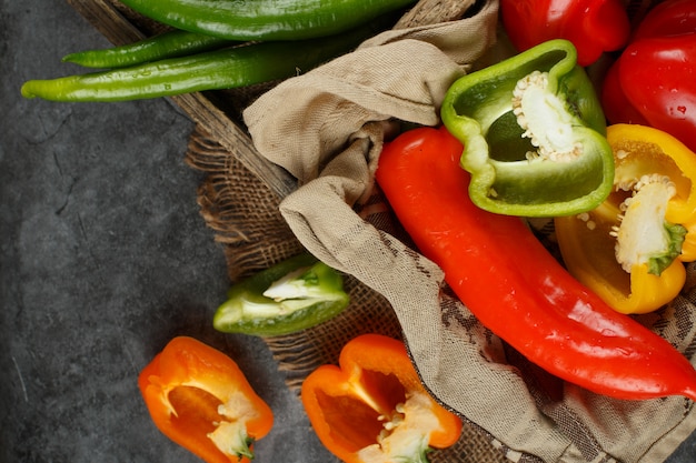 Free photo whole and half cut peppers in a rustic tray. top view.