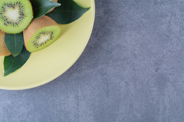 Whole and half kiwi fruits on plate on marble table.