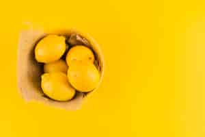 Free photo whole lemons in the bowl with jute fabric on yellow background