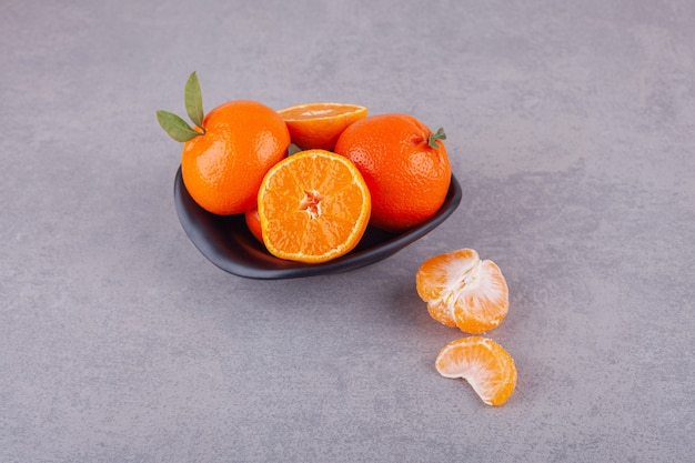 Whole orange fruits with green leaves placed on plate. 