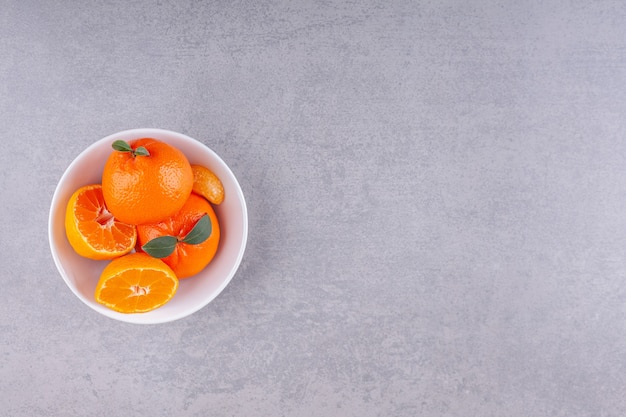 Whole orange fruits with green leaves placed on white plate.