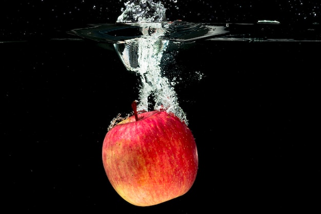 Whole red apple falling in water over black background