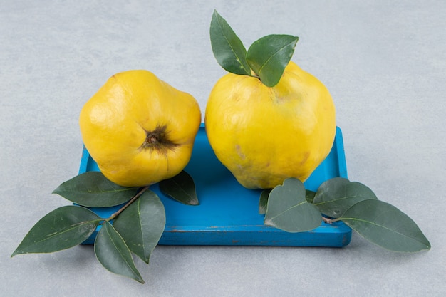 Free photo whole ripe quinces with leaves on blue plate