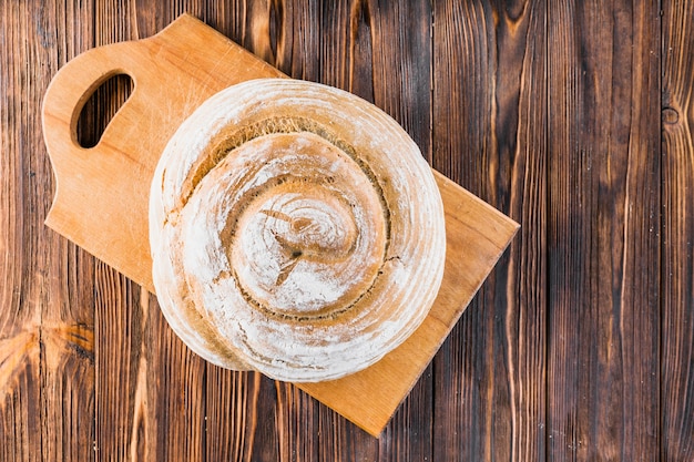 Whole round baked bread on chopping board over the wooden background