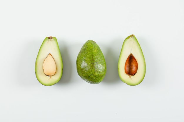 Whole and sliced avocado on a white surface. top view.