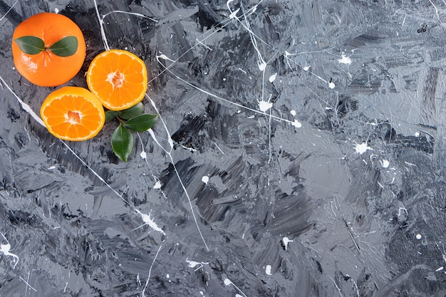 Free Photo whole and sliced fresh orange fruits with leaves placed on a marble table.