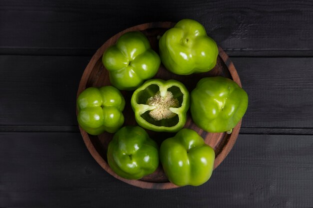 Whole and sliced green bell peppers placed on wooden dark table . High quality photo