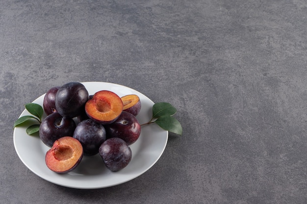 Free Photo whole and sliced juicy red plum fruits placed on a white plate