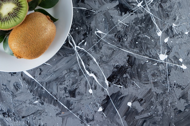 Free Photo whole and sliced kiwi fruits with leaves placed in a white plate.