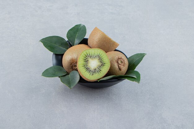 Whole and sliced kiwis in black bowl. 