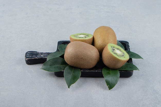 Whole and sliced kiwis on black cutting board. 