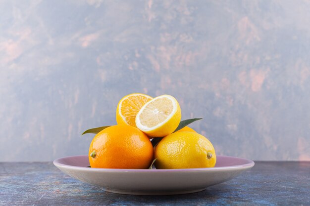 Whole and sliced lemon fruits with leaves placed on stone table.