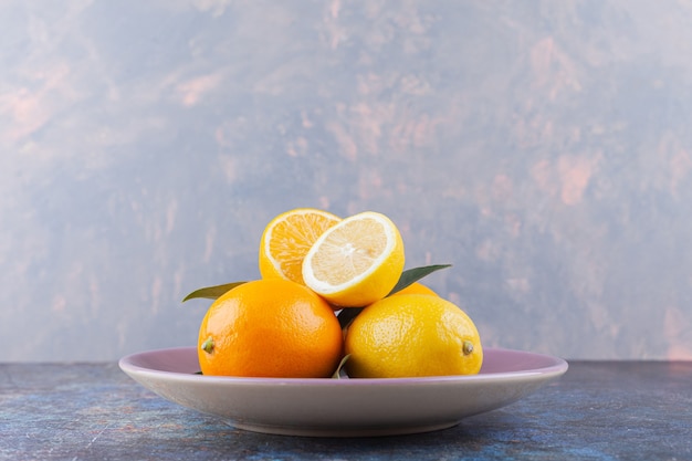 Whole and sliced lemon fruits with leaves placed on stone table.