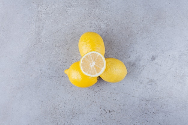 Whole and sliced lemon fruits with leaves placed on stone table.