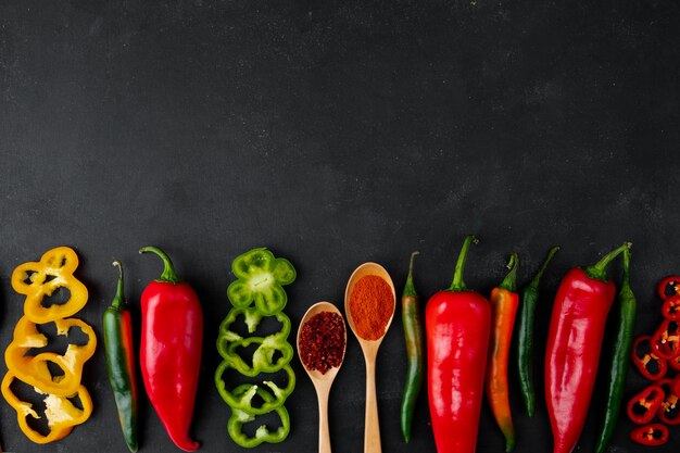 whole and sliced peppers with spices on black table