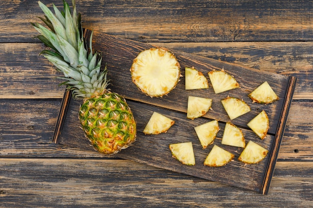 Free photo whole and sliced pineapple in a wood piece on a old wood grunge surface. flat lay.