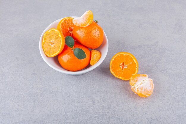 Whole and sliced tangerine fruits with leaves placed on a stone table.