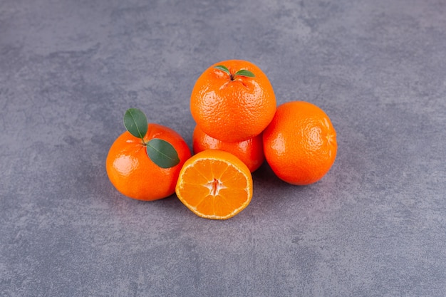 Whole and sliced tangerine fruits with leaves placed on a stone table.