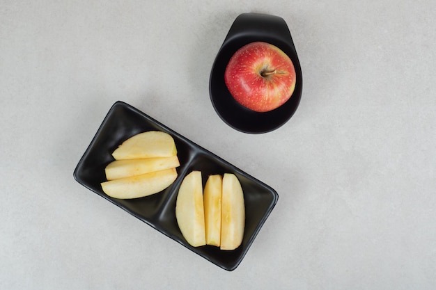 Whole and slices of red apple on black plates. 