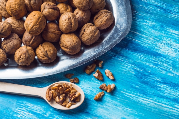 Free Photo whole walnuts and kernel on tray and wooden spoon on blue painted backdrop