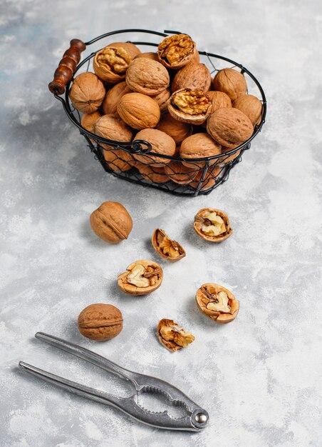 Whole walnuts in shell in food metal basket, walnut kernels. Top view on concrete 