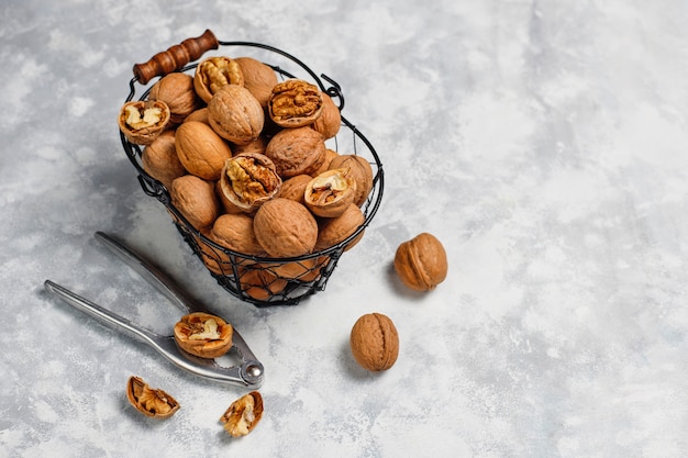 Whole walnuts in shell in food metal basket, walnut kernels. Top view on concrete 