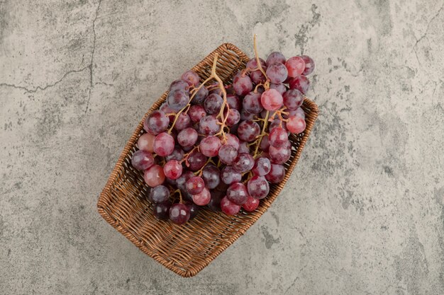 Wicker basket of delicious red grapes on marble table. 