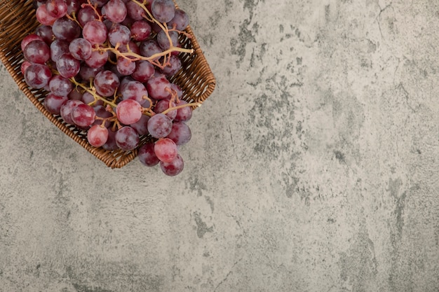 Free photo wicker basket of delicious red grapes on marble table.