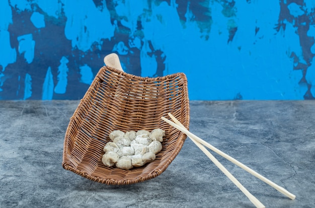 Free Photo a wicker basket of raw dumplings and chopsticks.