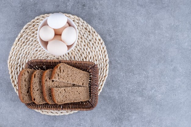 Wicker basket of rye bread and bowl of raw eggs on stone table.