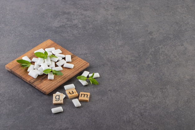 Wide angle photo of pile of white gums with mint leaves on wooden bowl