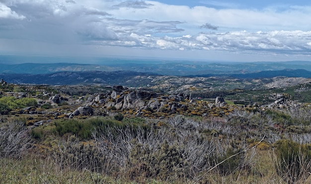 Wide angle shot of a large rocky and grassy field with clouds in the sky