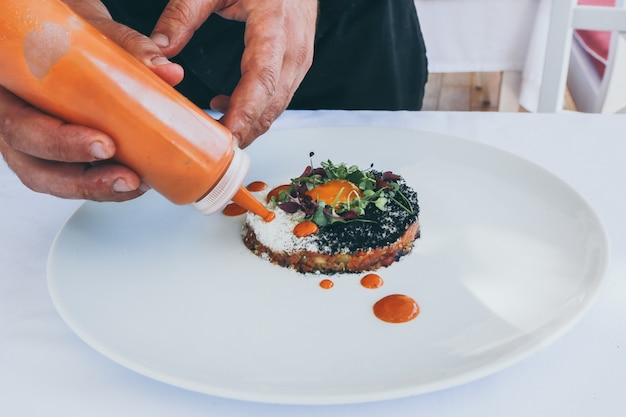 Free photo wide closeup shot of a person pouring ketchup on a cooked meal on a white plate