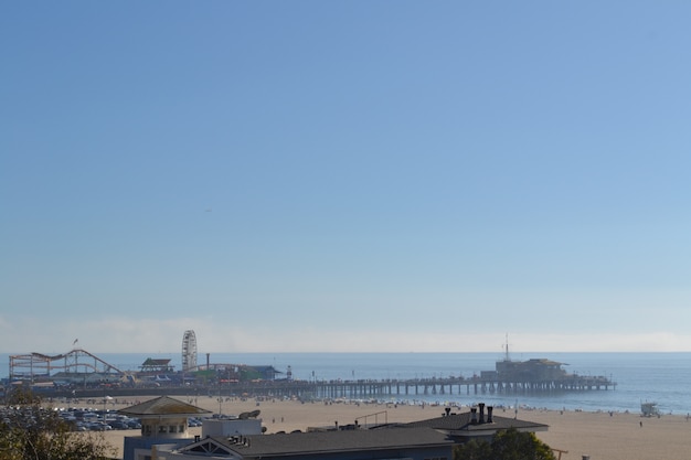 Free Photo wide distant shot of an amusement park on a dock by the sea under a clear blue sky